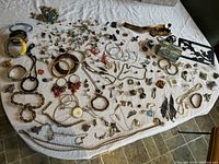 Full view of assorted costume jewelry on white cloth showing necklaces, bracelets, earrings and brooches scattered across surface.