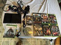 Full layout photo showing PS2 console, various games including Xbox One Anthem, World of Warcraft CD, cables, microphone, and controller.