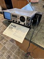 Full view of Sony TV-413 with attached antenna and instruction manual laid flat on the table. Unit has a blue speaker grille and retro styling.