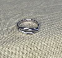 Close-up image of sterling silver ring on fabric background showing open overlapping design and interior marking.
