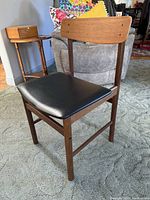 Full view of the teak Danish chair showing the black leather seat and the natural teak wood frame and curved backrest.