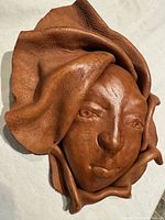 Front view showing detailed human face carved in brown leather with folds around the edges