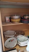 Shelf with ceramic and glass baking dishes, aluminum bundt and springform pans, and a Black & Decker hand mixer box visible at bottom edge.