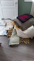 Overview of bedding linens, blankets, throws piled on floor showing various colors and textures.