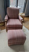 Front view of vintage reupholstered chair with matching ottoman showing pink striped upholstery and wooden armrests.