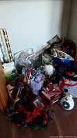 Photo of assorted Christmas decorations including teddy bear on bench, snowman figures, Father Christmas, gift bags and wrapping paper.