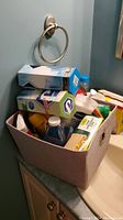 View of fabric storage bin filled with cleaning supplies and boxed bulb on countertop beneath towel ring