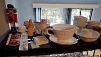 Full view of decorative and kitchen items on a dark wooden console table including the nutcracker, bowls, gravy boat, dog figurine, and covered jars