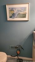 Framed print of a flying white heron on a blue wall, with metal heron sculpture on the floor beneath it.