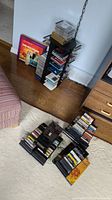 Photo of a black metal CD stand holding various compact discs and cassette tapes on wooden floor.