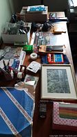 Overall lot on wooden surface showing pens, rulers, mouse, clips, paper, light and framed art