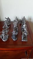 Overall group shot of the twelve pewter figurines arranged on a wooden surface.