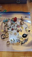 Overhead view of assorted jewelry pieces in a zip-loc bag including cameo earrings, animal pins, studs and assorted bits