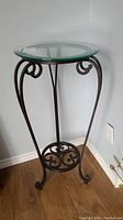 Full view of wrought iron plant stand with glass top from a side angle showing curled legs and circular lower support.