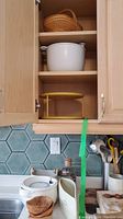 Open cupboard with white ceramic soup tureen on middle shelf and yellow lazy Susan stand on bottom shelf