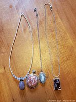 Full view of all four sterling silver necklaces laid out on wood surface showing variety of pendants and chains.