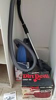 Blue Miele canister vacuum with hose and wand alongside Dirt Devil Handy 150 box