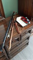 View of all items on wooden dresser including two walking canes, back scratcher, and two sheathed Highland Sgian Dubh knives.