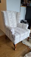 Front and side view of vintage wingback chair showing light floral and stripe upholstery and wooden legs.