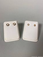 Two pairs of stud earrings displayed on white velvet earring cards; left card has pearl earrings and right card has opal flower-shaped earrings.