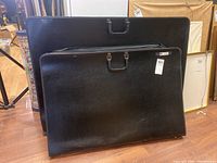 Three black vintage portable art portfolio bags stacked together showing size differences and wear