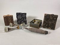 Lot overview showing three carved wooden printing blocks, the icing syringe and nozzle set in metal box, pair of glass door knobs, and wooden bobbin spool with thread.
