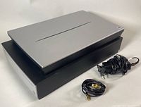 Closed view of silver lid and black base with cables beside unit