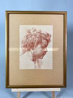 Full view of framed art showing child's profile sketch in red monochrome with beige mat and gold frame.