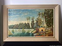Full view of framed oil on board painting showing landscape scene with river, palm trees, and stone building.