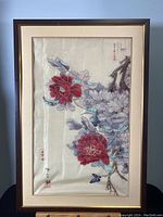 Frontal view of the framed watercolour painting depicting red and purple flowers with branches and Chinese calligraphy, surrounded by beige mat and dark brown frame.