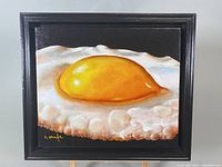 Full view of framed oil painting depicting a fried egg on black background.