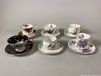 Six vintage teacup and saucer sets arranged in two rows showing detail and variety of designs and colors.