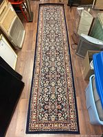 Full view of long rectangular hand knotted runner rug with intricate floral design and borders on wooden floor.