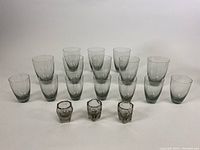 Front view of all smoked glassware pieces grouped by size including 8 large, 7 medium, 3 small tumblers, and 3 small hexagonal cups arranged in rows.