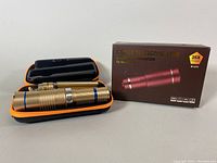 Metallic gold telescopic lens, protective black and orange case, and original product box featuring product image and lens magnification details.