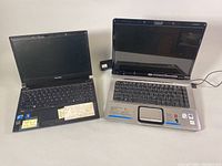 Two laptops side by side on a white surface, left is Toshiba Tecra R700 black laptop with screen open and visible keyboard, right is HP Pavilion dv6000 black and silver laptop with screen open.
