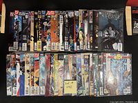 Photo showing 50 comic books arranged in two rows, featuring multiple superhero titles and characters from Marvel and DC comics.