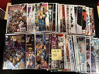 Photo showing approximately 50 comic books arranged in two rows, each bagged and boarded, featuring Justice League and various Marvel and DC superheroes.