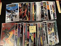 Photo showing a collection of approximately 50 bagged and boarded comic books arranged in stacks. Characters and series include Batman, Green Arrow, Wonder Woman, and others.