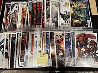 Photo of approximately 50 comic books arranged flat, showing various titles and covers, all bagged and boarded, predominantly Marvel and DC titles including Avengers, X-Men, and Justice League.