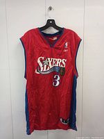 Front view of red Allen Iverson Philadelphia 76ers basketball jersey with number 3 and Sixers logo.