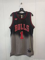 Front of black and grey gradient Derrick Rose Bulls basketball jersey with red and white lettering and Adidas logo.