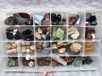 Top view of large assortment of diverse rocks and minerals organized in a plastic storage box with 40 individual compartments, showing variety in size, color, and texture.