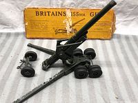 Front angle showing the Britains 155mm toy army gun with original yellow box in background, visible paint wear, black rubber wheels.