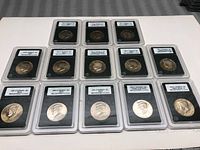 Overview photo showing all 13 Kennedy half dollar coins in certification slabs arranged in two rows on a white surface.