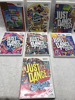 Seven Nintendo Wii game cases arranged on white fabric surface, covering the full lot.