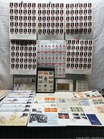 Full view of multiple sheets of stamps featuring Queen Elizabeth II on top, commemorative seals sheets in the middle, and first-day cover envelopes spread below.