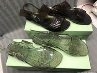 Two pairs of jelly sandals on green shoe boxes, one clear translucent and one dark translucent, showing overall style and color.