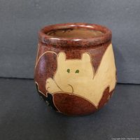 Front angle view of small pottery vase showing cat design in beige on reddish-brown background.