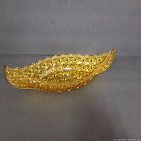 Top view of amber glass canoe-shaped decorative dish showing floral textured pattern and curved shape.